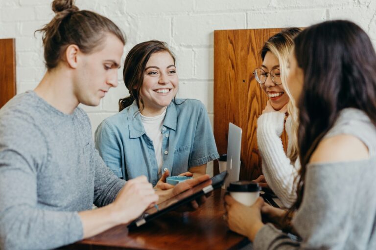 A group of four happy employees share a coffee amidst a meeting around a wooden table