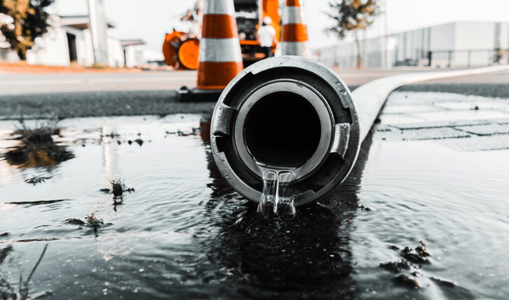 Water leaks from a metal pipe into a puddle in the street