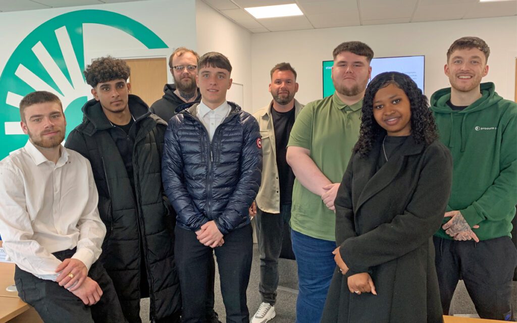 Eight new starters colleagues standing in front of a large Procure Smart branded wall