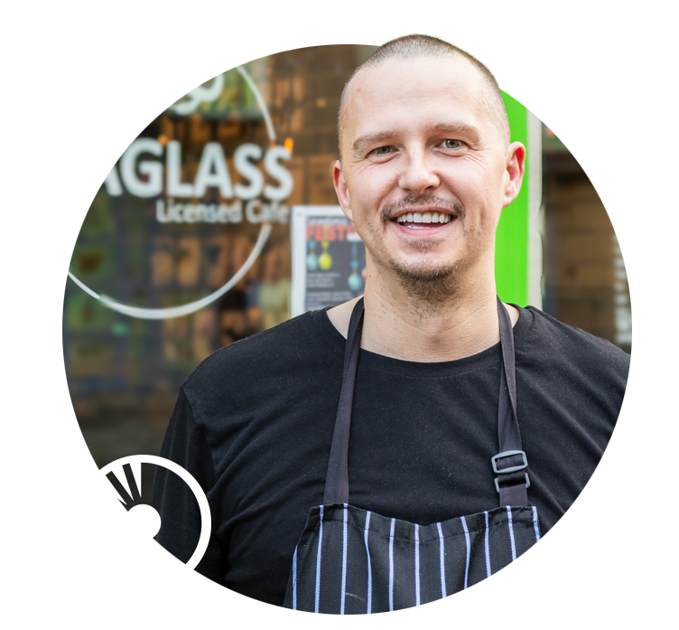 Man stands in front of his cafe window, showing the Seaglass Cafe Logo