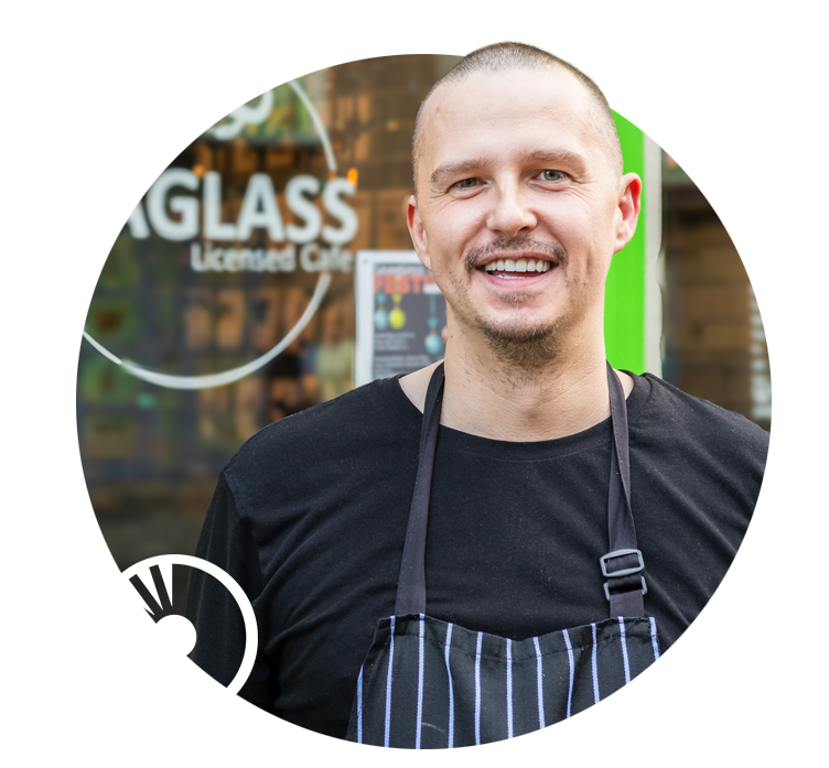 Man stands in front of his cafe window, showing the Seaglass Cafe Logo