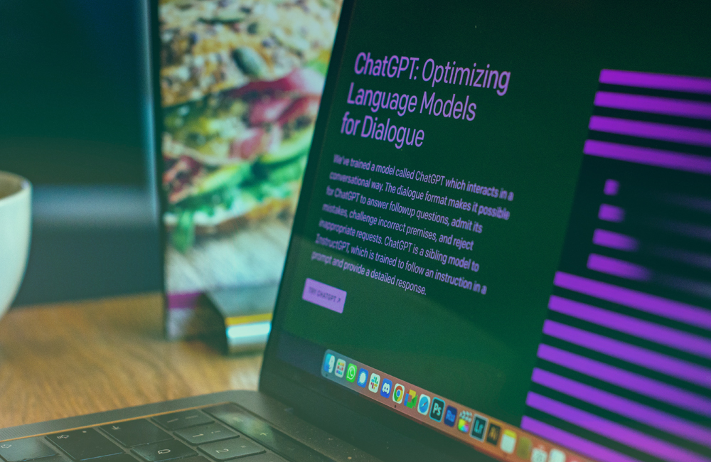 A laptop open on a table, showing the homepage of ChatGPT with the title "optimising language models for dialogue"